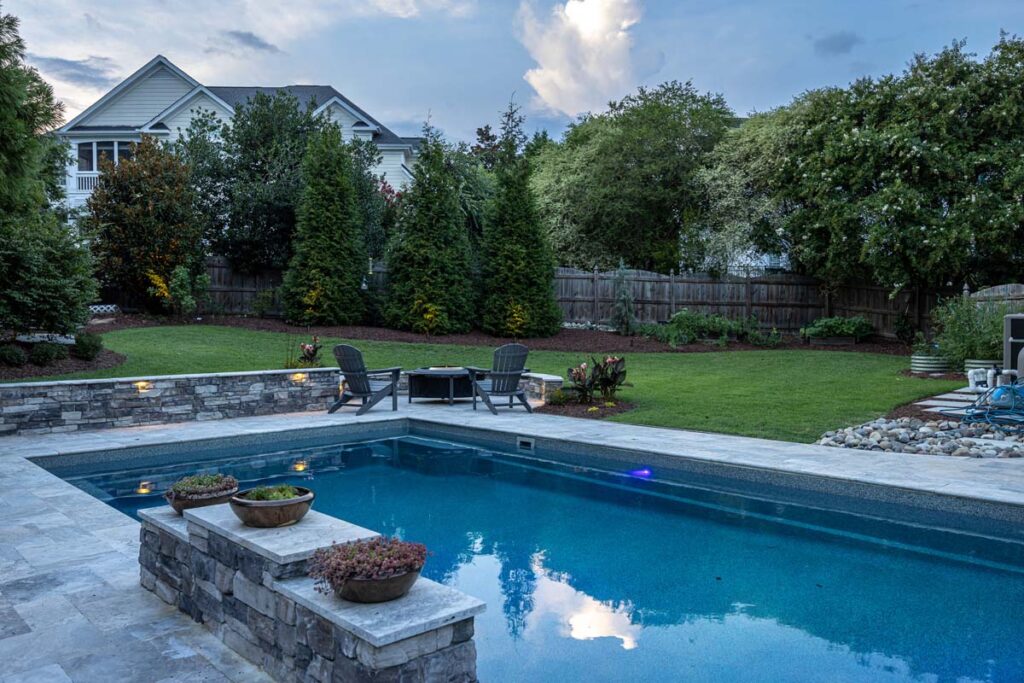 Dominion pool featuring pool lighting, fire pit, and retaining wall.