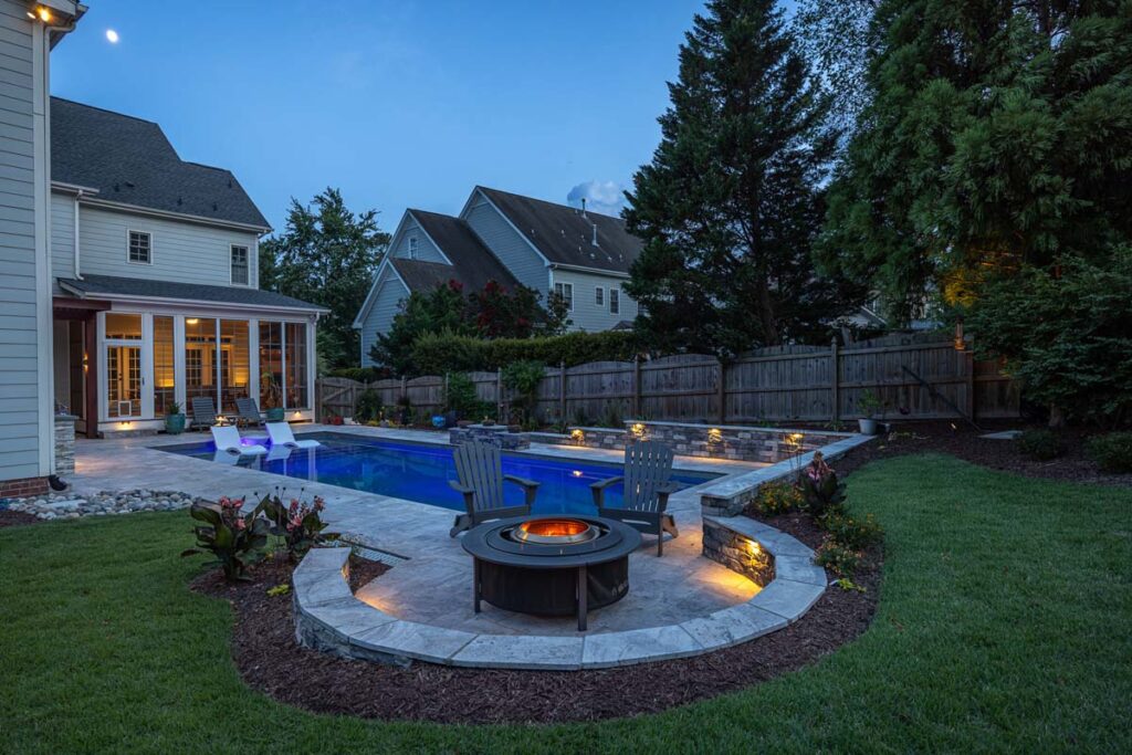 Dominion pool area, deck, fire pit, low-voltage lighting and retaining wall at night.