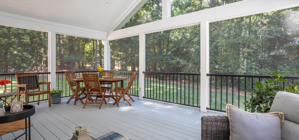 Interior wide shot capturing interior of Lowery screen porch, with plentiful areas to gather including chairs and dining area on the left and couch on the right.