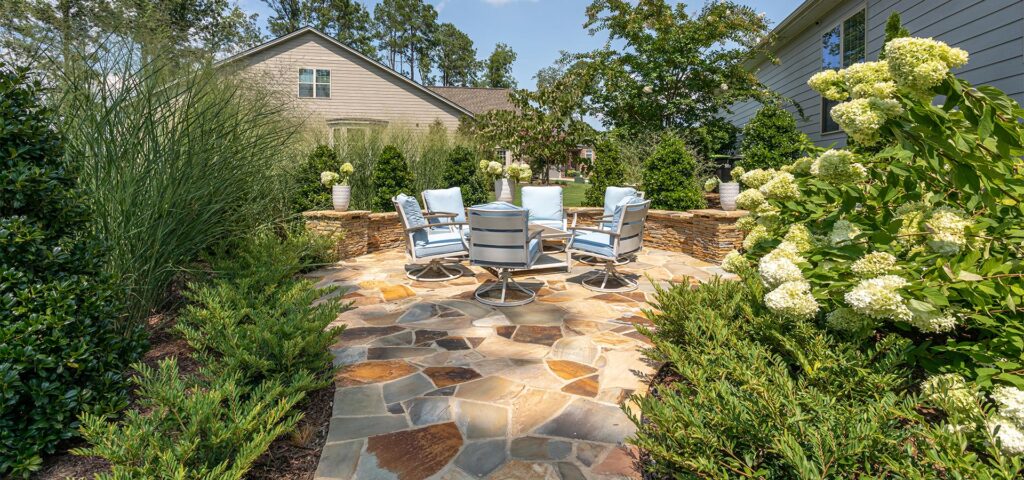 Silver Dew project features patio, landscaping and retaining wall services. Wide shot of gathering area surrounded by beautiful garden and a semi-circle retaining wall.